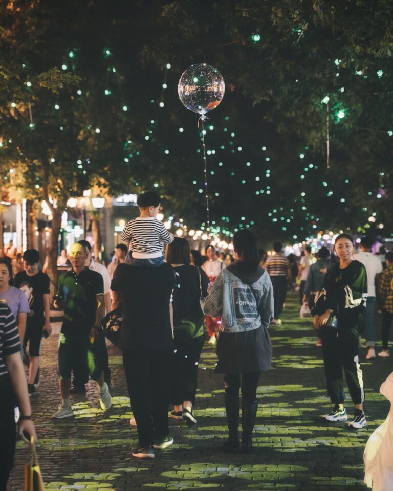 A lively street festival at night with people enjoying and celebrating under string lights.